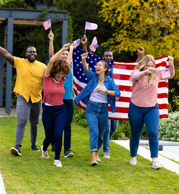 Happy diverse friends holding flags of usa and walking in garden. Independence day, fourth of july, patriotism, friendship, flags and lifestyle, unaltered.